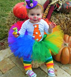 a baby dressed up as a clown sitting in front of pumpkins