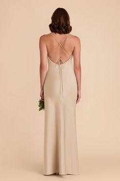 the back of a woman wearing a beige dress with straps and a flower in her hand