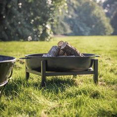 a fire pit sitting in the middle of a field next to a metal bowl filled with logs