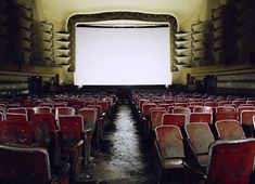 an empty auditorium with rows of red seats and a large screen on the wall above it