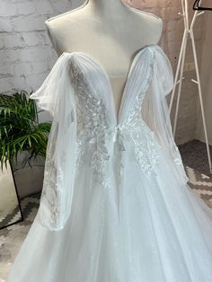 a white wedding dress on display in a room with a mirror and potted plant