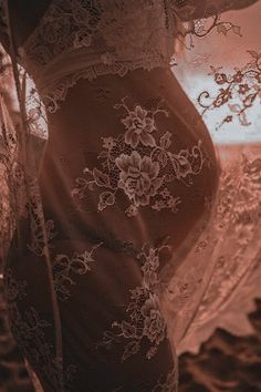 a pregnant woman is standing in the sand with her belly covered by lacy fabric and lace