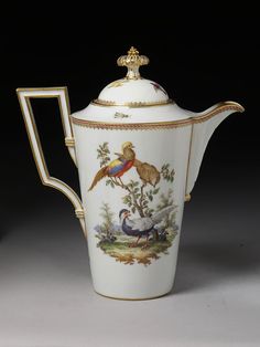 a white tea pot with birds painted on the side and gold trimming around it