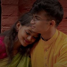 a young man and woman embracing each other in front of a brick wall with red bricks behind them