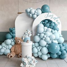 a teddy bear sitting in front of a balloon arch with blue balls and decorations on it