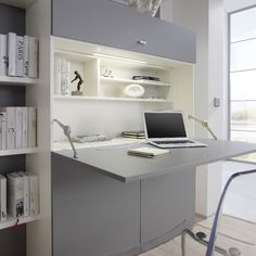 a computer desk sitting under a window next to a book shelf filled with lots of books