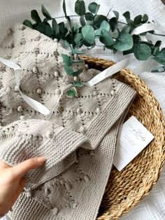 a basket filled with knitted sweaters next to green leaves and a hand pointing at the label