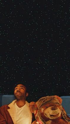 a man sitting on a bench with a stuffed animal in front of the stars above him