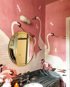 there is a mirror on the wall and two swans painted on the wall behind it