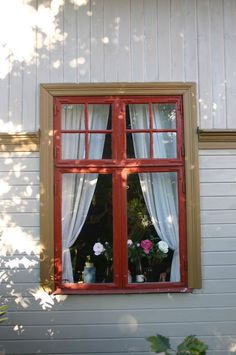 an open red window with white curtains and flowers