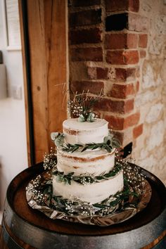 a three tiered cake with greenery on top is sitting on a wooden barrel