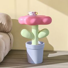 a pink and green plant in a white pot on the floor next to a couch