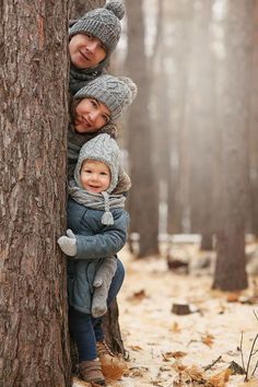 three children are hugging each other in the middle of a snowy forest with trees and leaves