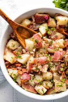 a white bowl filled with potato salad and a wooden spoon next to some parsley