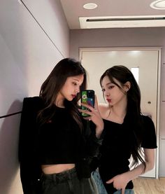 two young women standing next to each other in front of a mirror looking at their cell phones