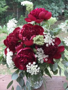 a vase filled with red and white flowers on top of a wooden table next to trees