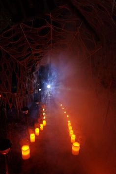 many lit candles are lined up in the middle of a dark tunnel with lights coming from them