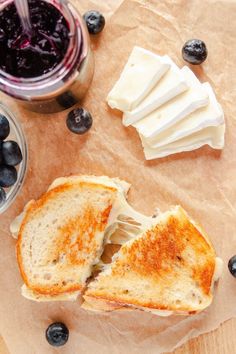 a sandwich cut in half with blueberries and butter on it next to a jar of jelly