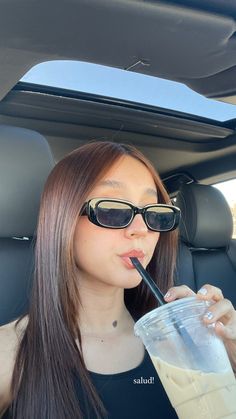 a woman drinking from a straw in the back seat of a car while wearing sunglasses