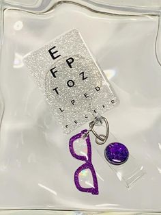 Eye chart badge reel with purple eye glasses charm. Approximately 2”. Easy to sanitize. Retractable swivel alligator clip. Each handmade item may show slight differences. Affordable Personalized Purple Badge Reel, Multicolor Retractable Badge Reel For Gift, Novelty Multicolor Badge Reel, Customizable Novelty Multicolor Badge Reel, Multicolor Retractable Badge Reel, Cute Badge Reel, Eye Chart, Work Friends, Glitter Eyes