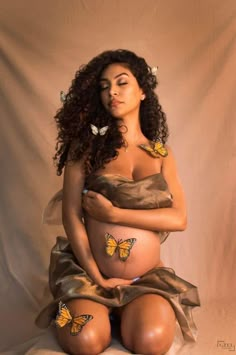 a pregnant woman with butterflies painted on her stomach, sitting in front of a white backdrop