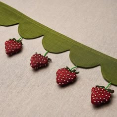 four tiny strawberries are hanging on a long green ribbon with white polka dot dots