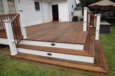 a wooden deck with steps and railings in front of a white house on the grass