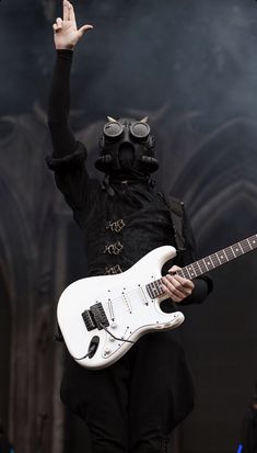 a person in a gas mask holding a white guitar and wearing a black outfit on stage