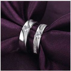 two white gold wedding rings with diamonds on top of each other in front of a purple cloth