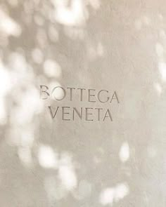 the words bottega veneta are etched in cement on a wall with trees