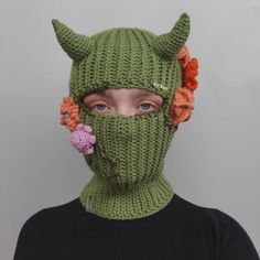 a woman wearing a green knitted mask with flowers on it's ears and nose