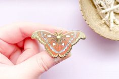 This beautiful Atlas Moth enamel pin features the gorgeous insect also known as Attacus atlas. Atlas moths are part of the Saturniidae family and can be found in tropical forests and shrublands in Asia. Atlas moths are some of the largest moths in the world, they can have wingspans of up to 9.4 inches. This hard enamel pin is 2.0" from tip to tip and features a beautiful palette of yellow, red, white and some gray accents. This hard enamel pin is set on a highly-polished gold-plated metal and ha Butterfly-shaped Enamel Pin Gift, Butterfly Shaped Enamel Pin For Gifts, Attacus Atlas, Large Moth, Moth Illustration, Atlas Moth, Tropical Forests, Tropical Forest, Hard Enamel Pin