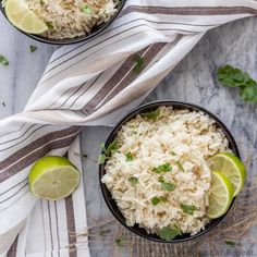 two bowls filled with rice, limes and cilantro on top of a marble table