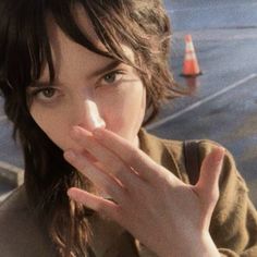 a woman is holding her hand up to her mouth and looking at the camera with an orange cone in front of her face