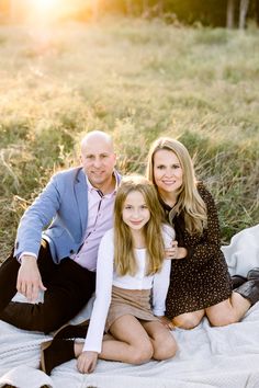 an adult and two children are sitting on a blanket in the grass, posing for a photo