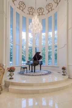 a grand piano in the middle of a room with large windows and chandelier