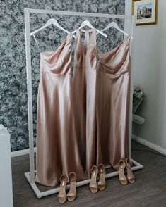 three bridesmaids'dresses hanging on a rack in front of a wallpapered background