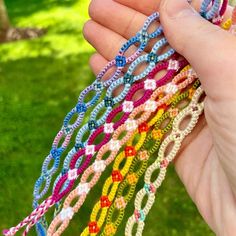 a hand holding several different colored bracelets in it's palm, with grass and trees in the background