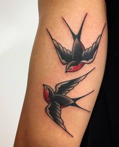 a couple of birds flying next to each other on a woman's arm with red and black ink