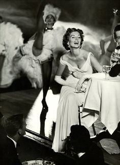 an old black and white photo of two people sitting at a table with wine glasses