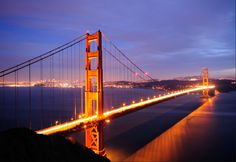 the golden gate bridge is lit up at night with lights on it's sides