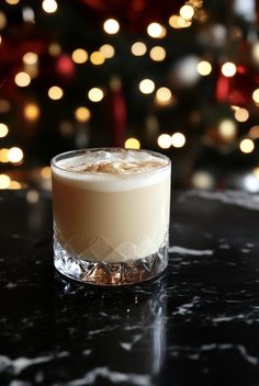 a glass filled with liquid sitting on top of a table next to a christmas tree