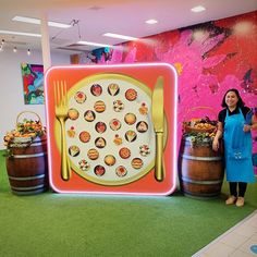 a woman standing in front of a table with food on it and two wooden barrels holding utensils