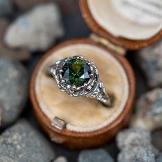 a ring with a green diamond in it sitting on top of some rocks and stones