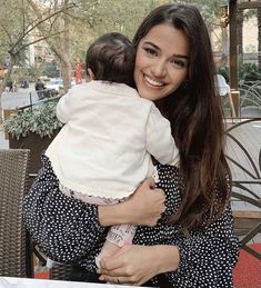 a woman sitting at a table with a baby in her arms and smiling for the camera