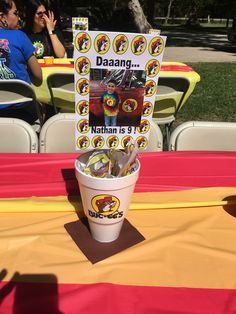 there is a bucket full of hot dogs on the table with people in the background