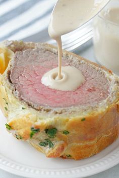 a piece of meat is being drizzled with mayonnaise on a white plate