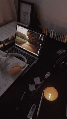 an open laptop computer sitting on top of a desk next to a lit candle and books