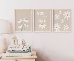 three framed pictures hang on the wall above a dresser with a stuffed animal and blanket