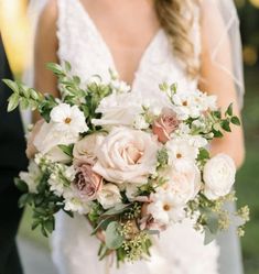 a bride holding a bouquet of white and pink flowers with greenery in her hand